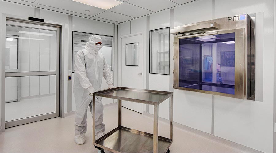Technician inside an Allied Modular cleanroom with pass-through chamber and stainless steel cart.