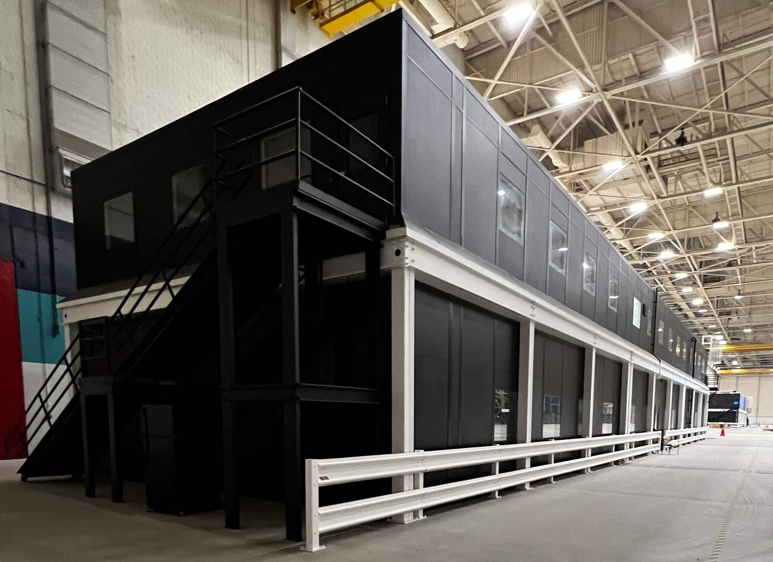 A black, two-story modular office building in a warehouse.