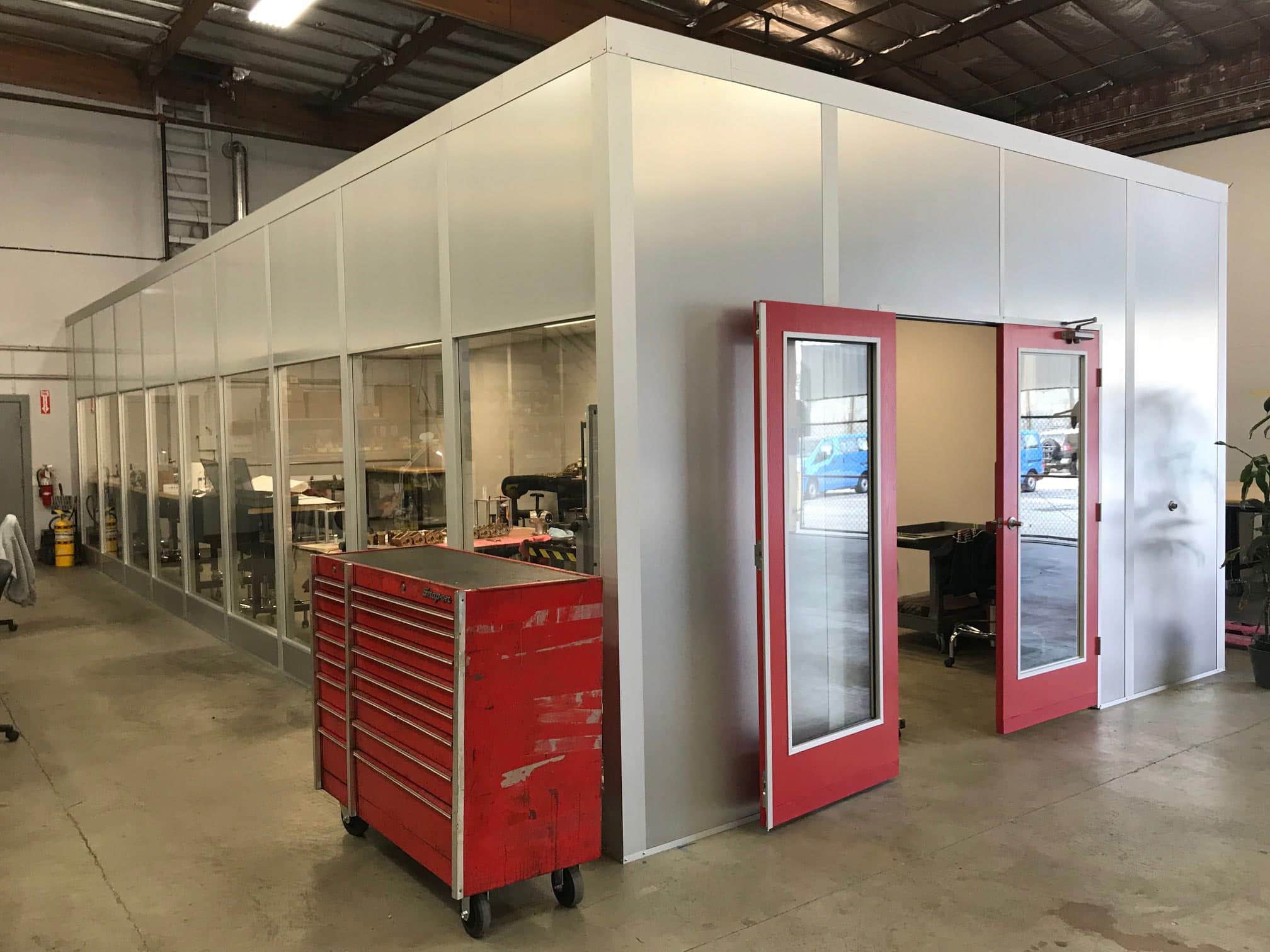 A modular office with glass windows and red doors installed inside a warehouse space.