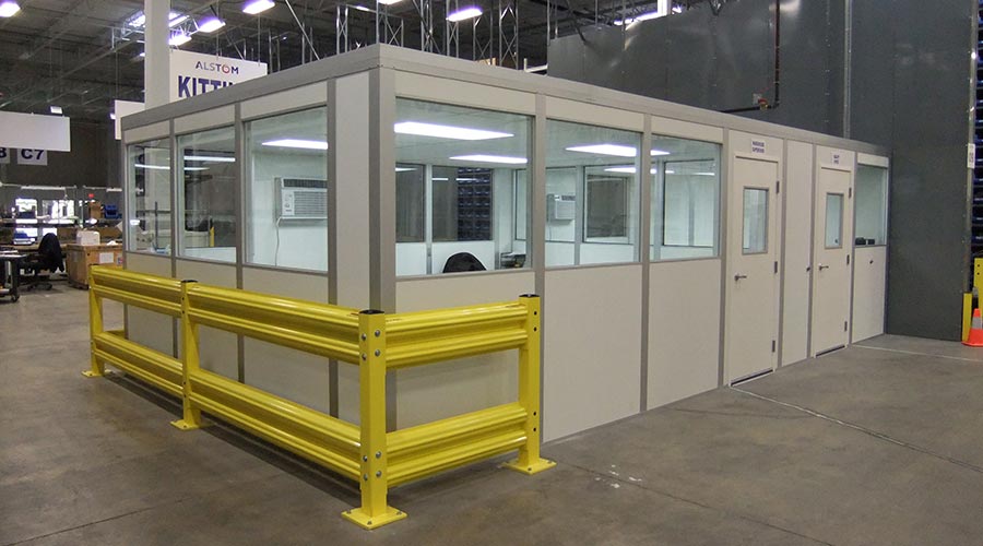 A modular building within a warehouse, serving as a dedicated office space with glass windows and secure entry doors.