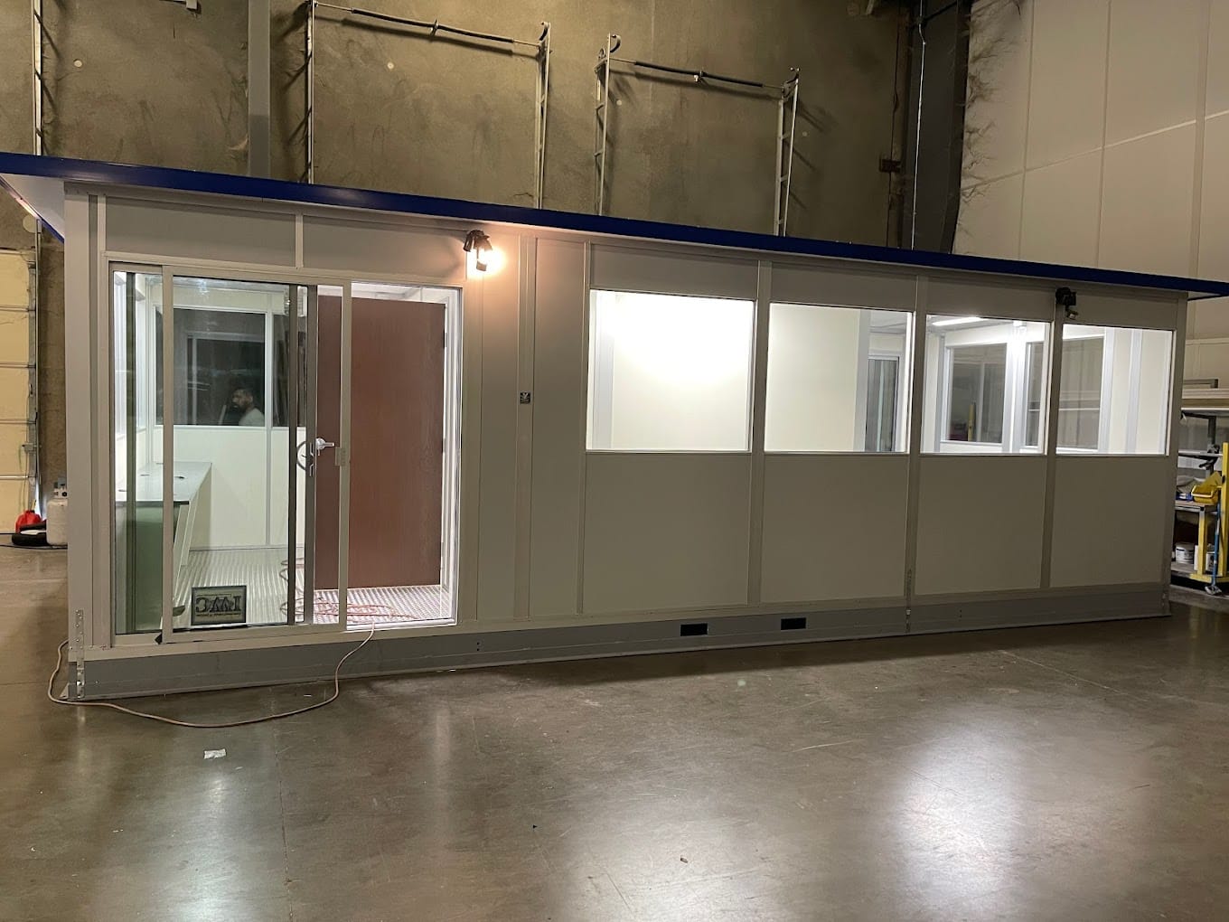 A modular office building with large windows and a door, assembled inside a warehouse.
