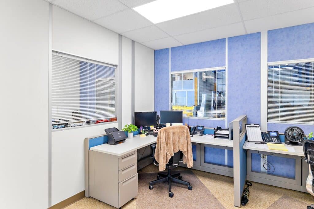 A modular office interior by Allied Modular, featuring a compact workspace with two desks, office equipment, and blue and white wall panels.