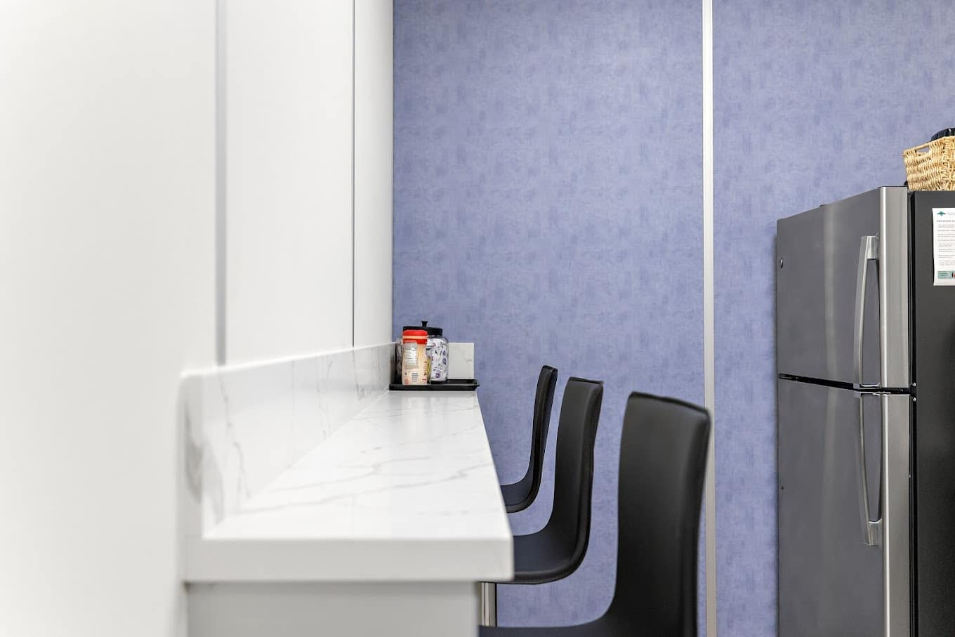 Inside a modular warehouse break room, with chairs, a refrigerator, and blue and white panels.