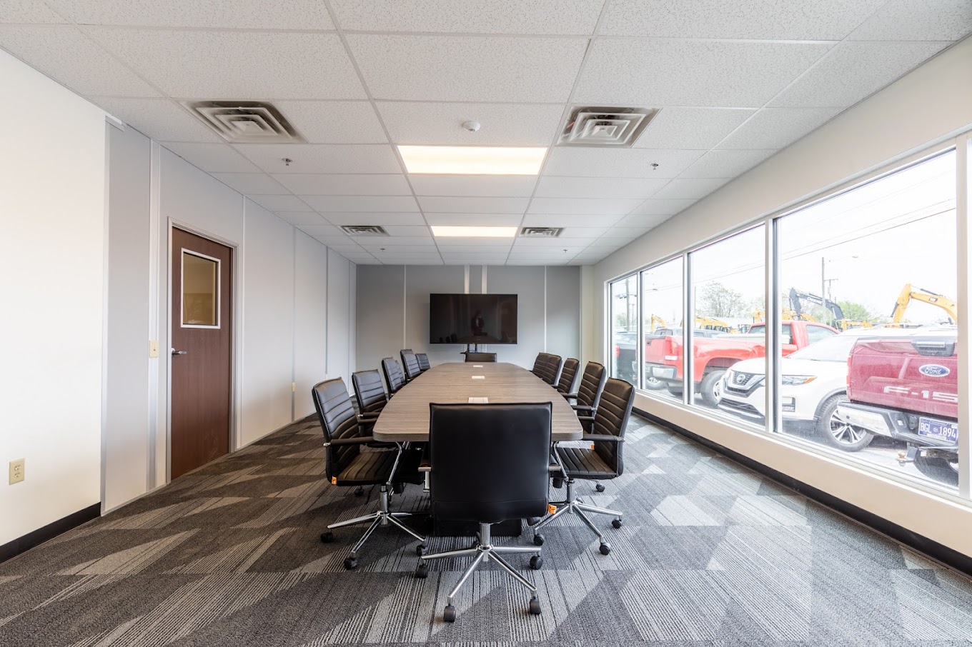 Spacious conference room with modern furnishings inside a modular office building, featuring large windows and a wall-mounted TV.