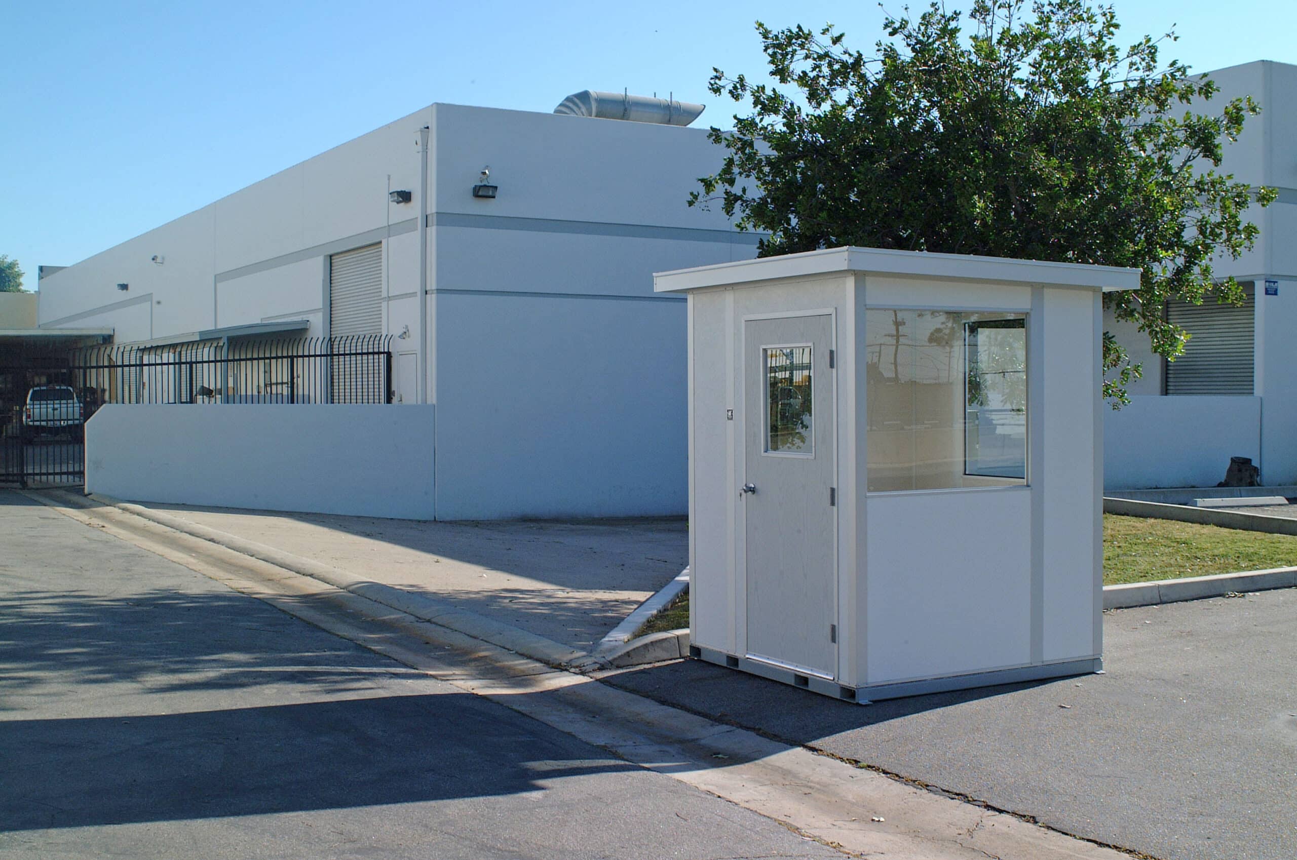 A small white warm-up booth located outdoors near an industrial building, featuring windows and a door.
