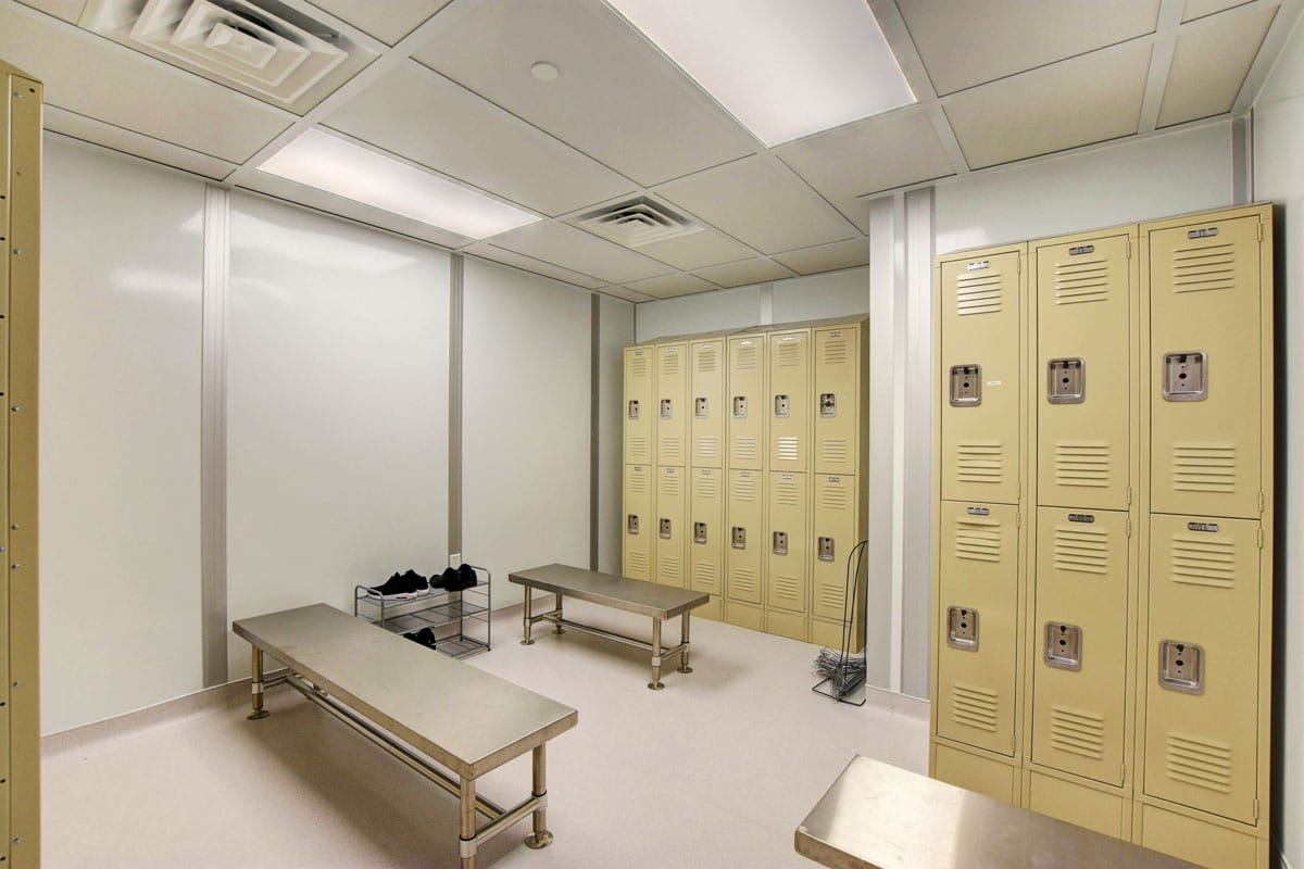 Modular locker room with stainless steel benches, beige lockers, and ceiling ventilation for controlled environments.