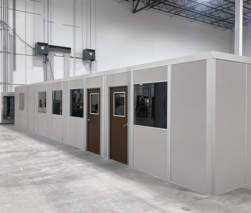 Modular inplant office installed in an industrial warehouse, featuring multiple doors, windows, and a clean, prefabricated design.