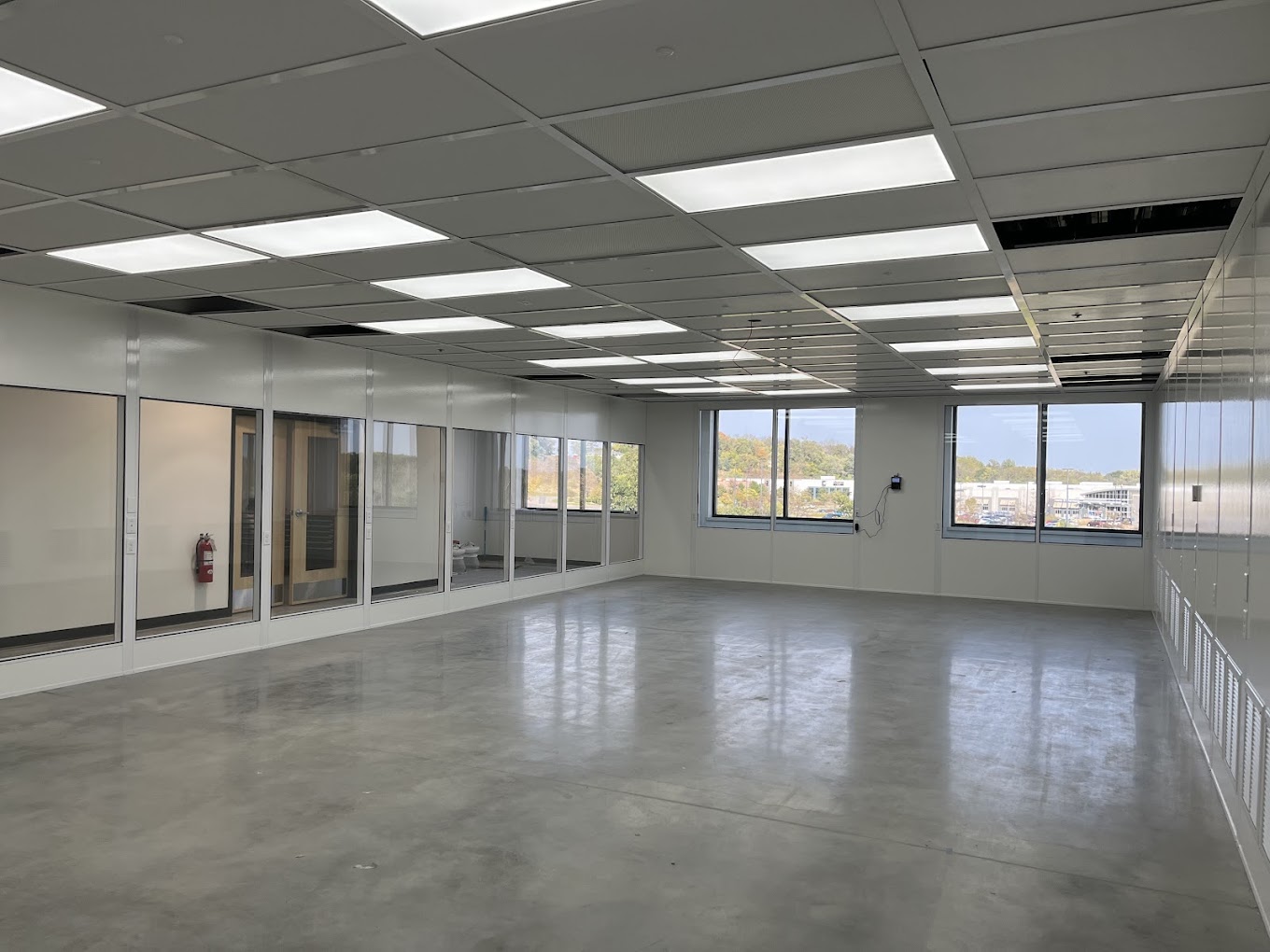 Spacious modular office interior with large windows, glass-paneled walls, and bright overhead lighting, showcasing a modern and versatile workspace design.