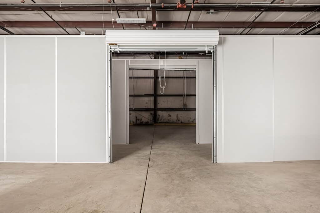 A warehouse space featuring a modular wall divider with an open roll-up door, allowing for easy access between separate areas.