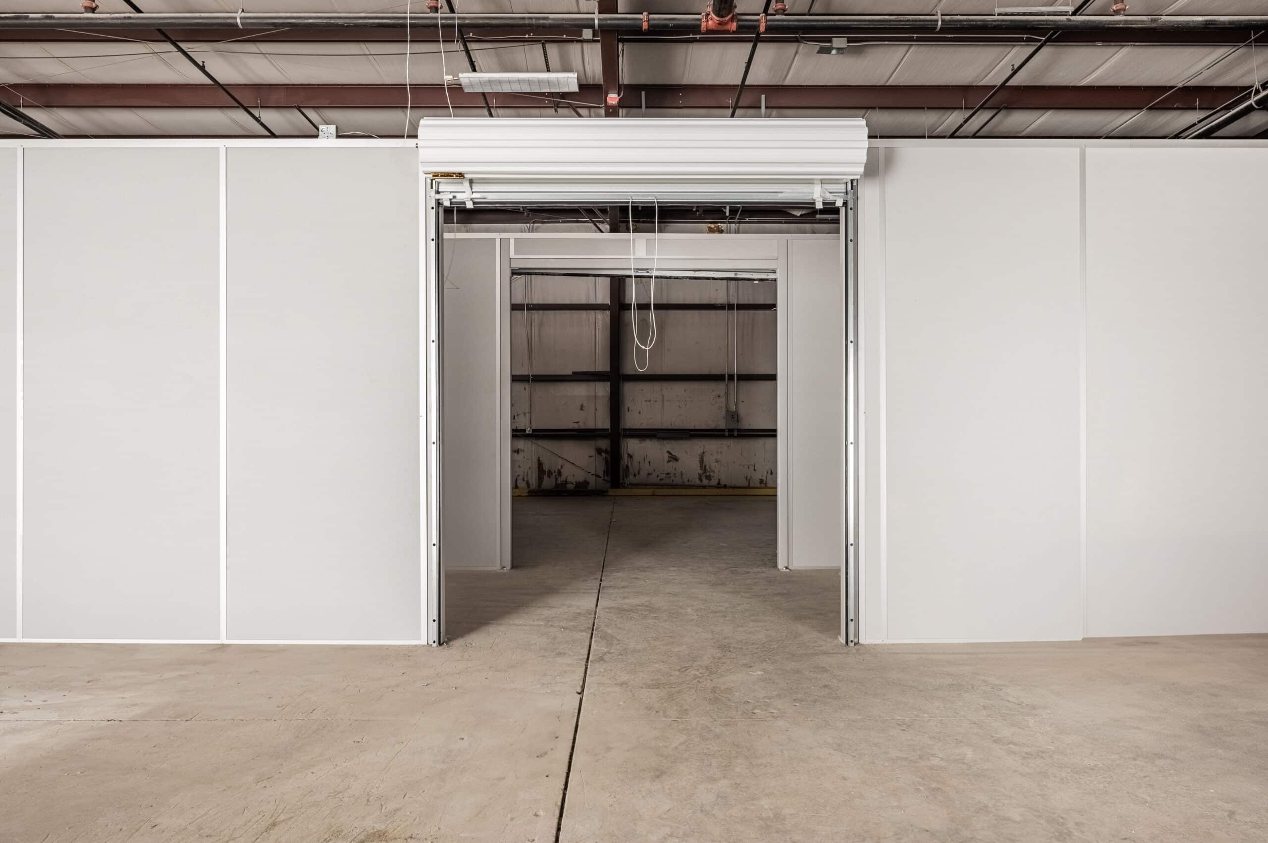 Modular warehouse partition with a roll-up door, dividing a large open space into smaller, customizable sections.