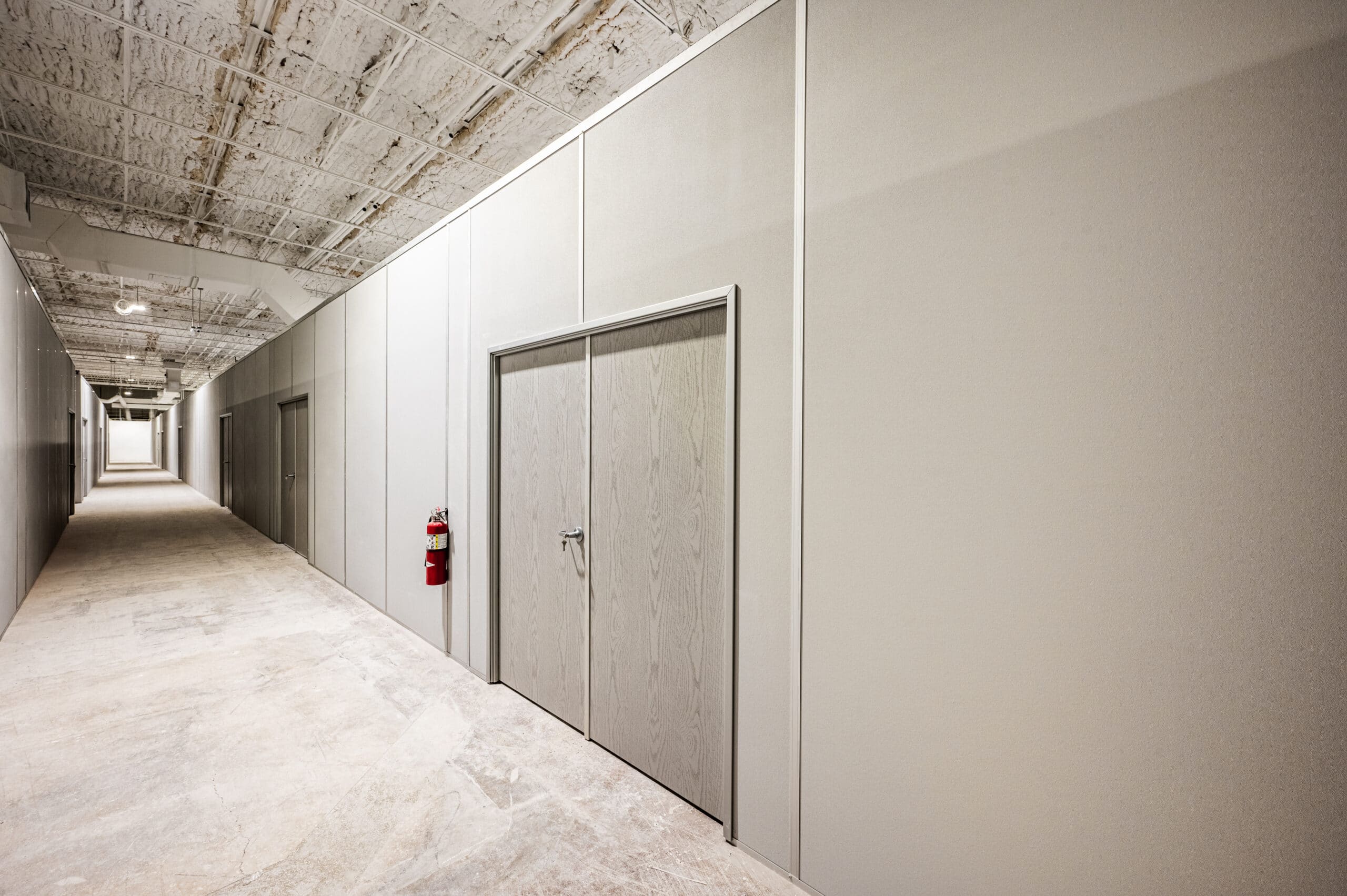 Warehouse interior featuring modular partition walls with a double door and a fire extinguisher mounted on the wall, showcasing a clean and organized layout.