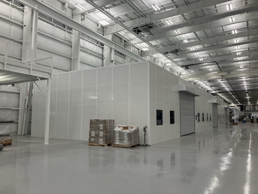 Modular warehouse enclosure with roll-up door and windows built by Allied Modular inside a large industrial facility.